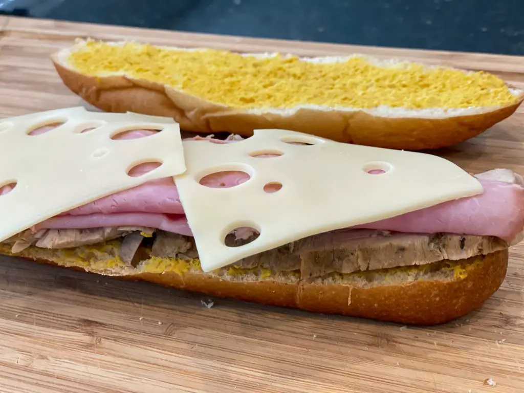 A Cuban sandwich consisting of pork, ham, cheese, pickles and mustard before it is cooked on a griddle (plancha). 