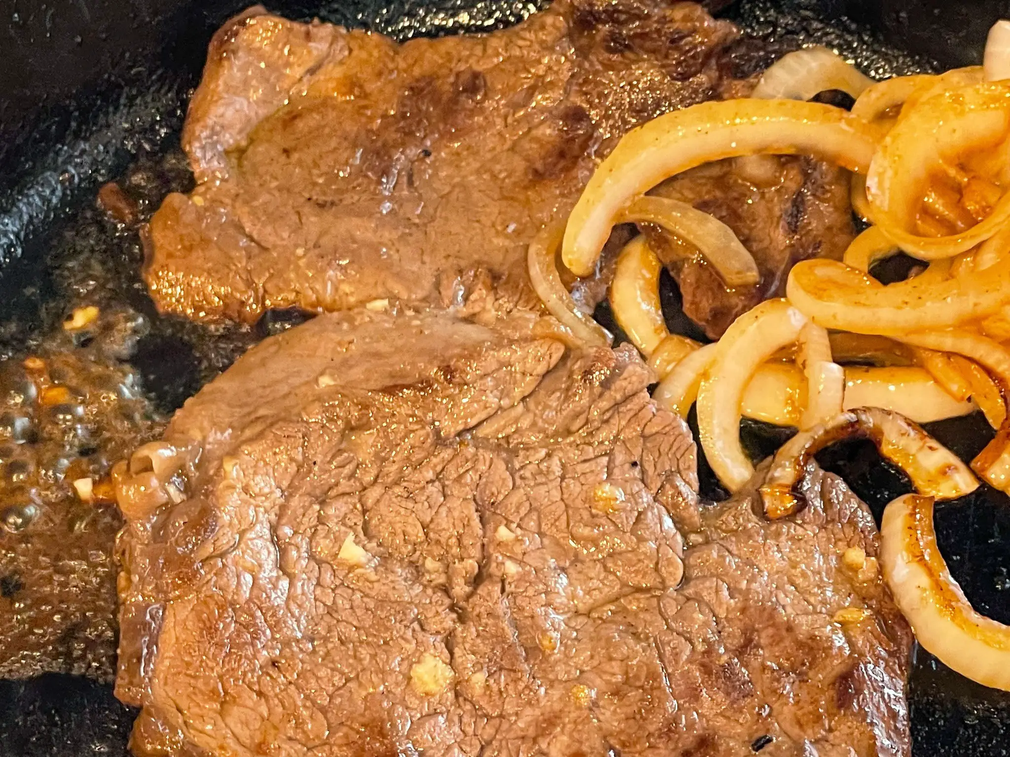 Cuban steak cooking with onions in a cast iron pan.