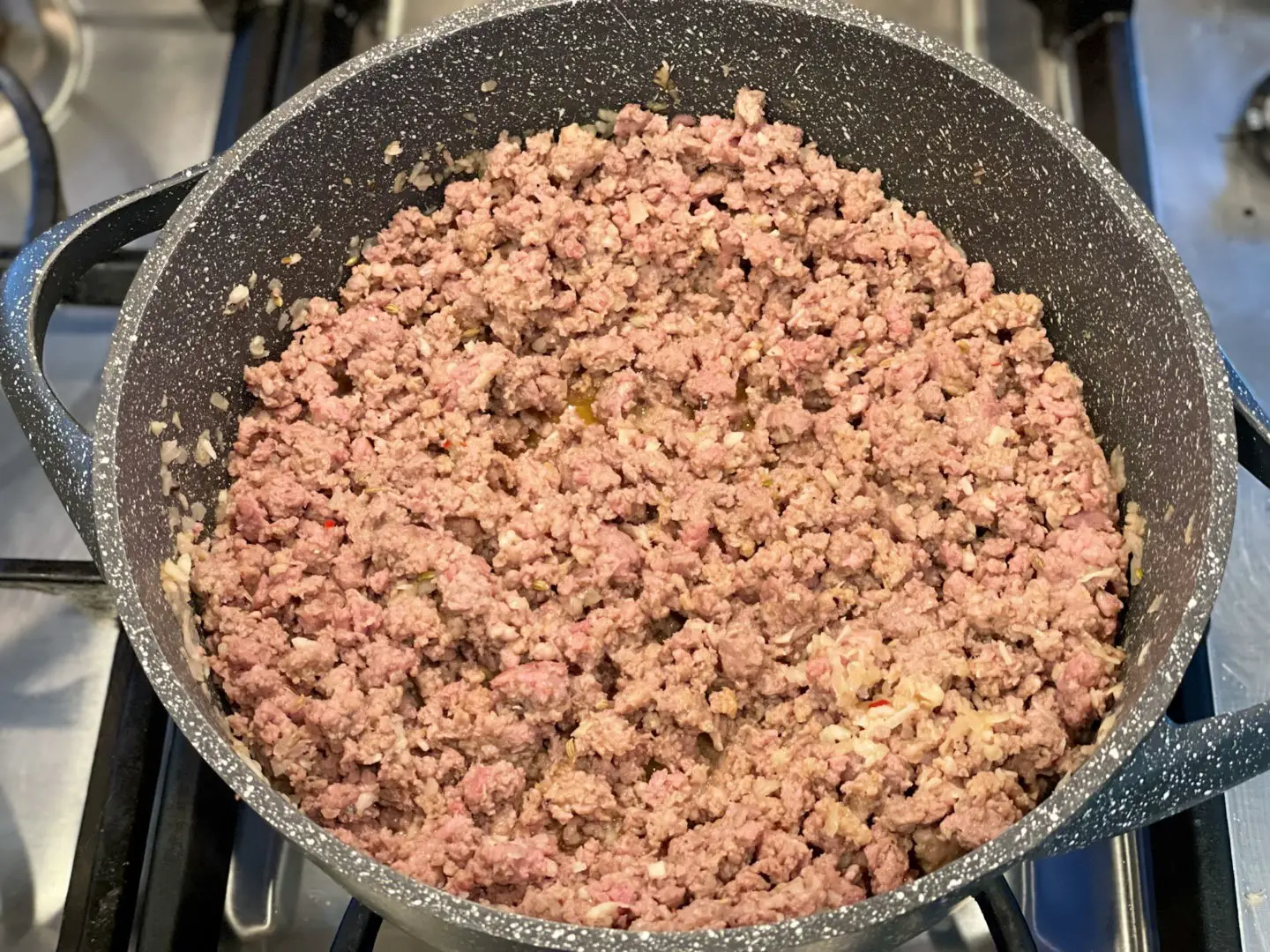 Browning meat sauce containing ground beef, Italian sausage and ham.