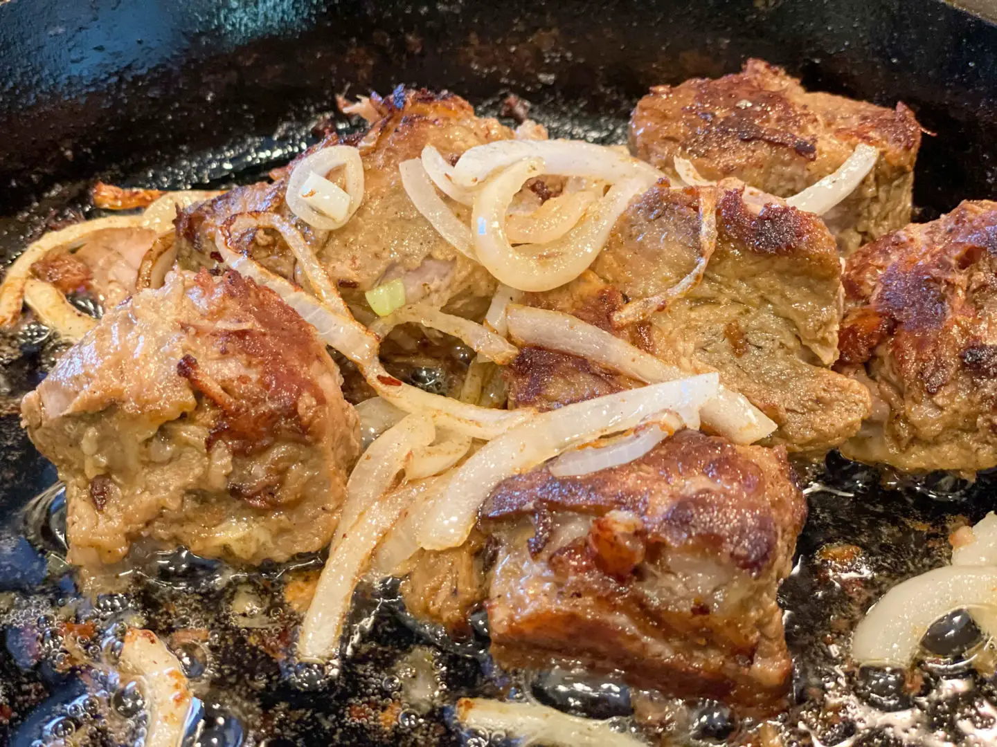 Masitas de puerco browning with onions in a cast iron skillet.