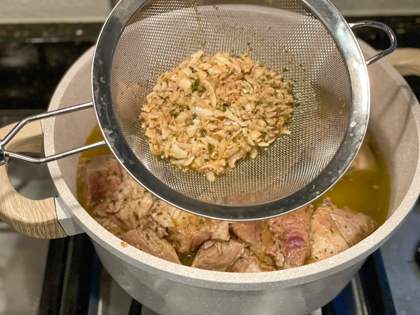 Adding mojo criollo to pork chunks straining out the garlic.