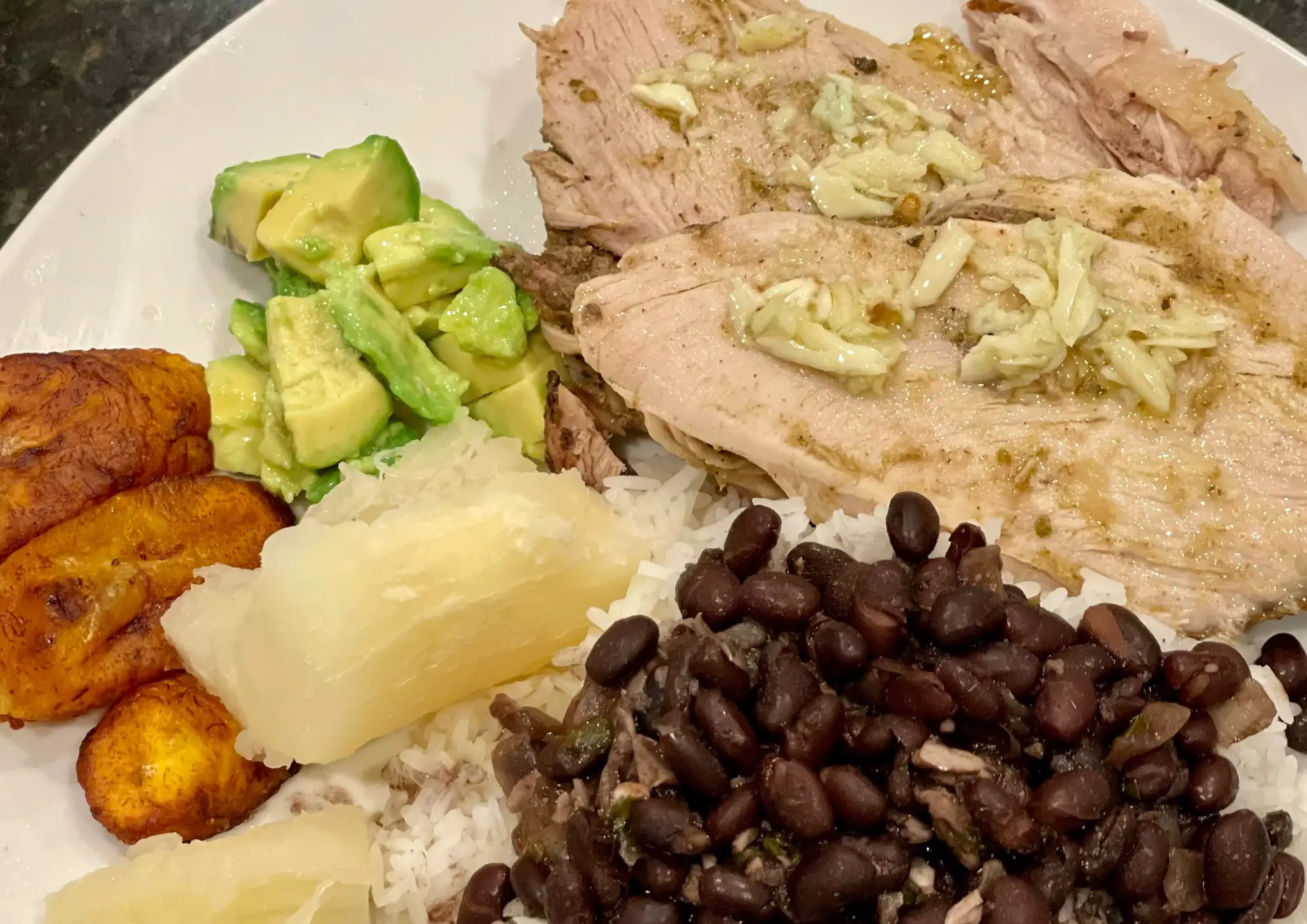 Traditional lechon dinner with lechon, black beans and rice, yuca, maduros and avocado.