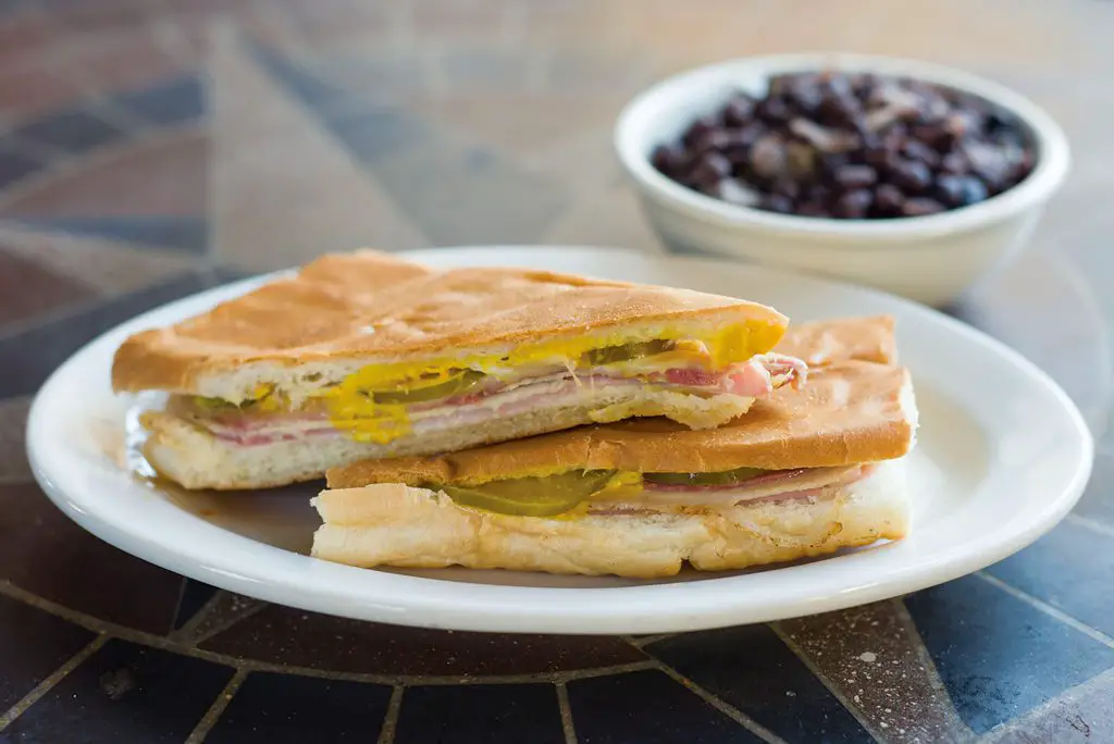 A Cuban sandwich served with a cup of black beans.