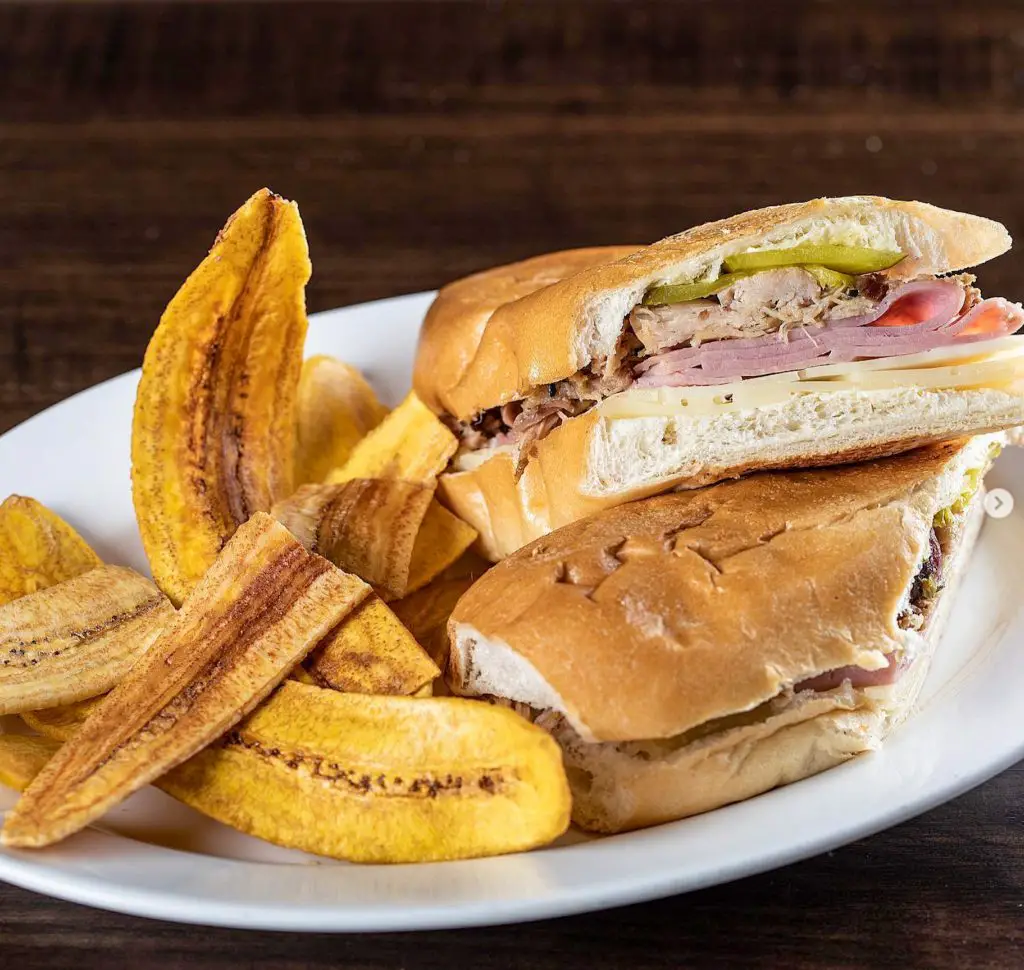 Cuban sandwich served on a plate with strips of fried plantains. 