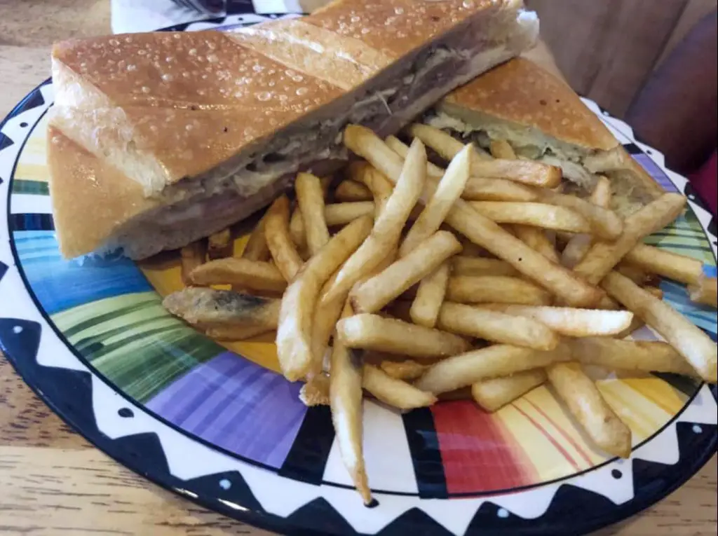 A Cuban sandwich cut in half served with french fries on a colorful plate.