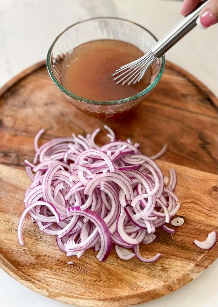 Thinly sliced red onions with pickling liquid on a board.