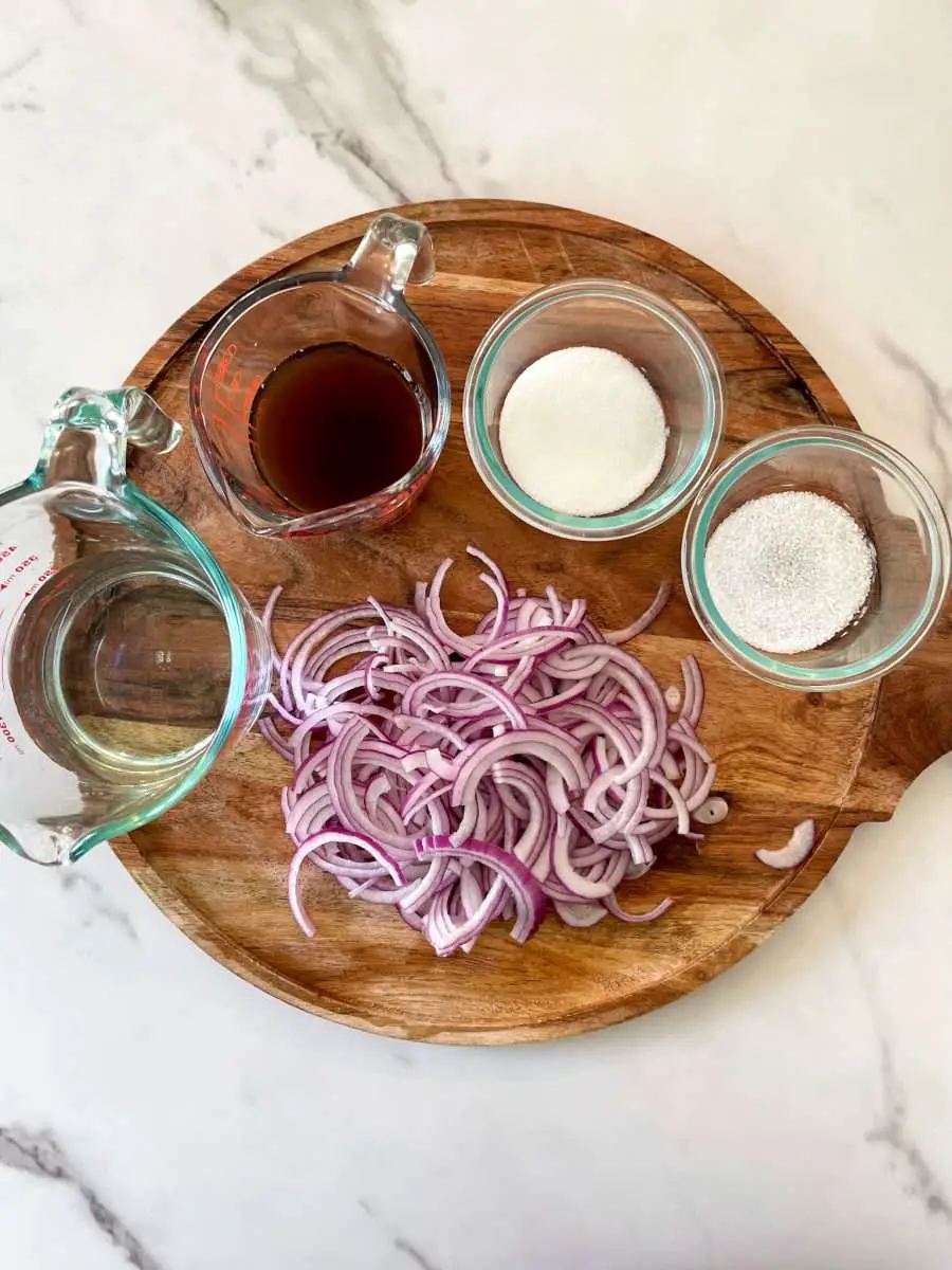 Thinly sliced red onions with pickling ingredients on a board.