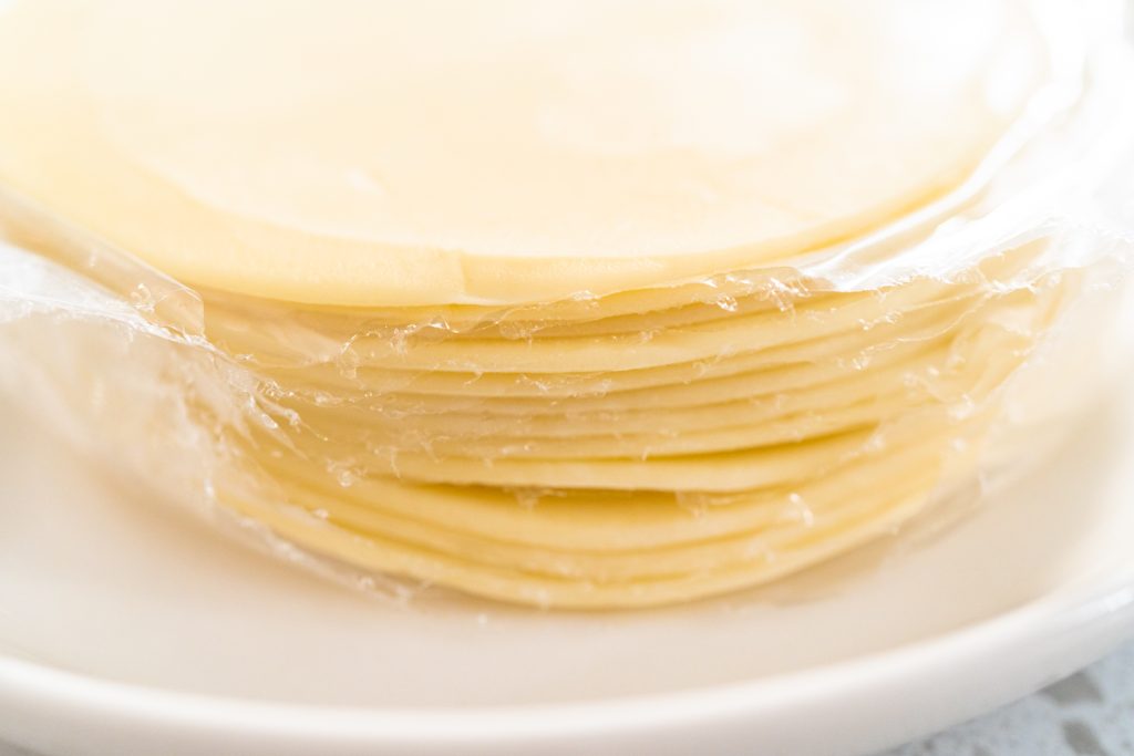 Empanada dough cut into discs stacked using plastic wrap to keep them separated.