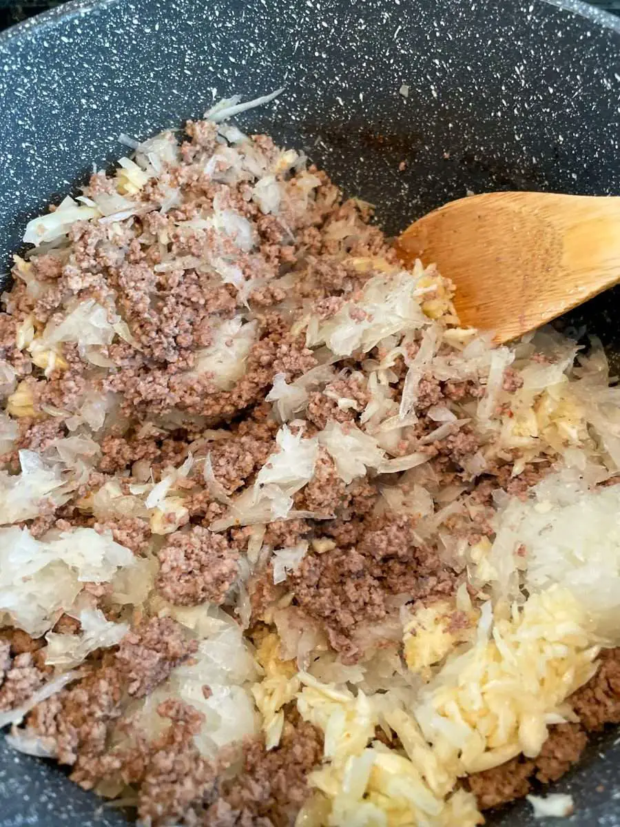 Adding grated onions and smashed garlic to Picadillo.