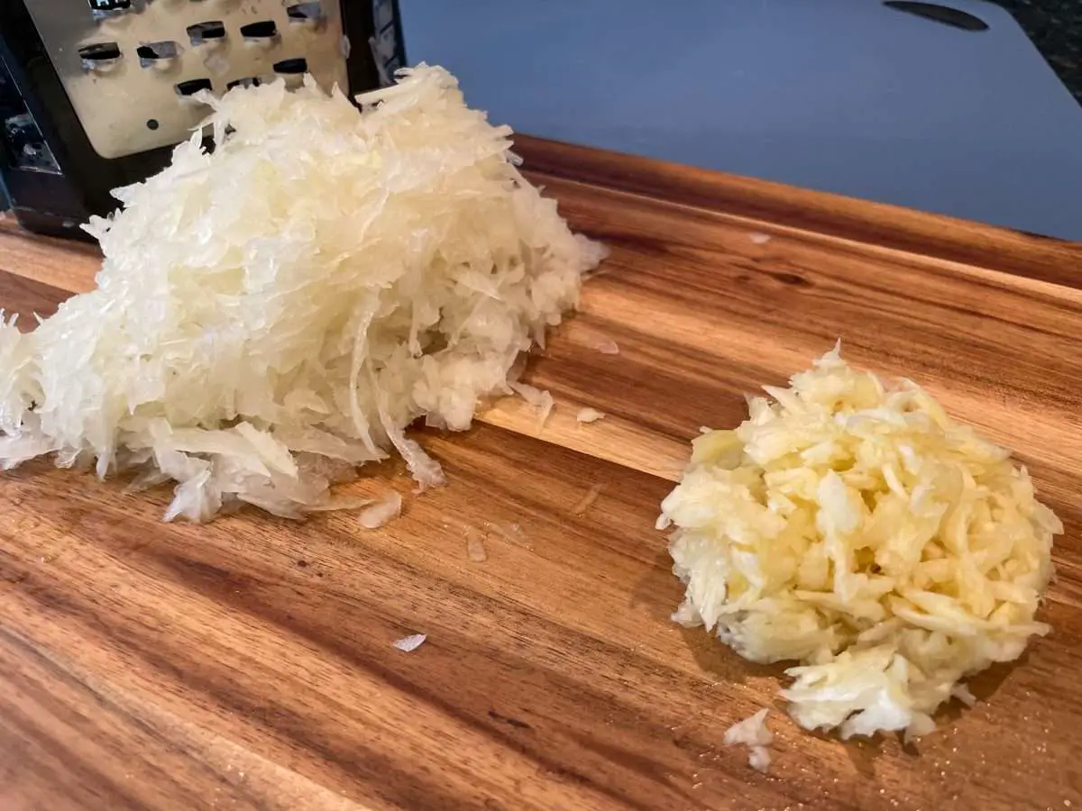 Grated onions and smashed garlic on a cutting board.