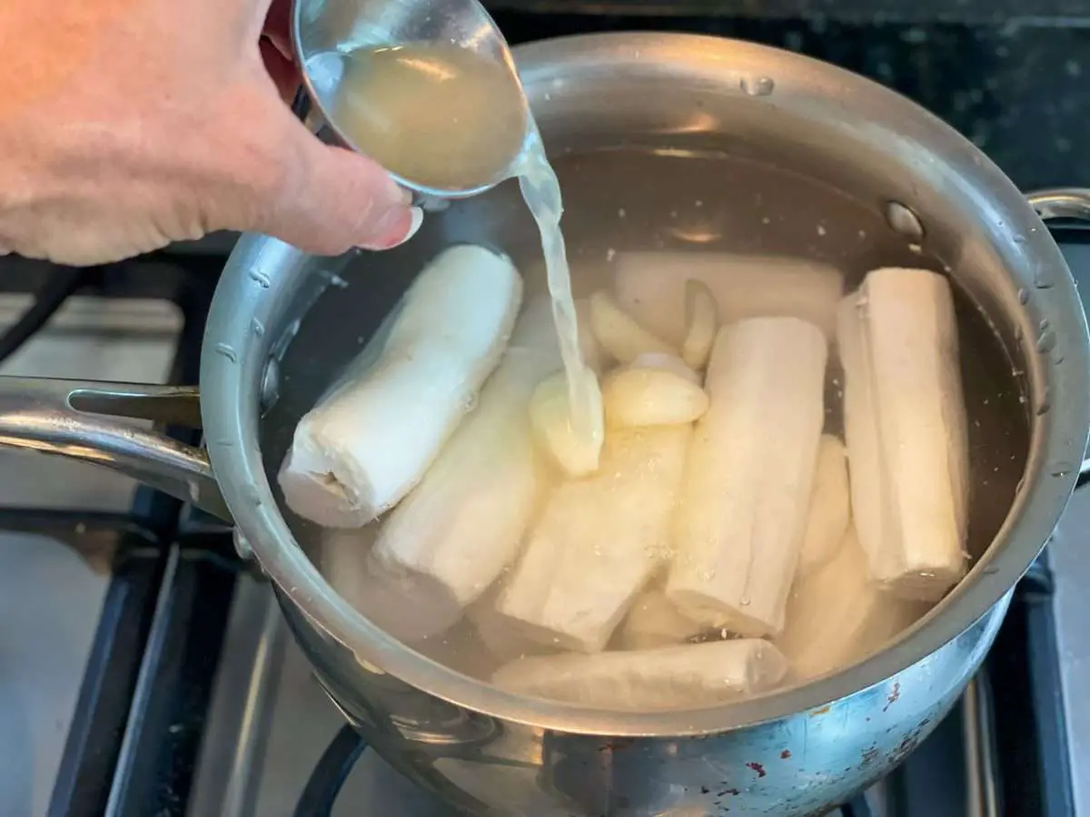Adding lime juice, garlic and salt to yuca in a pot.