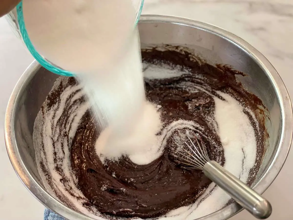 Adding sugar to brownie batter.