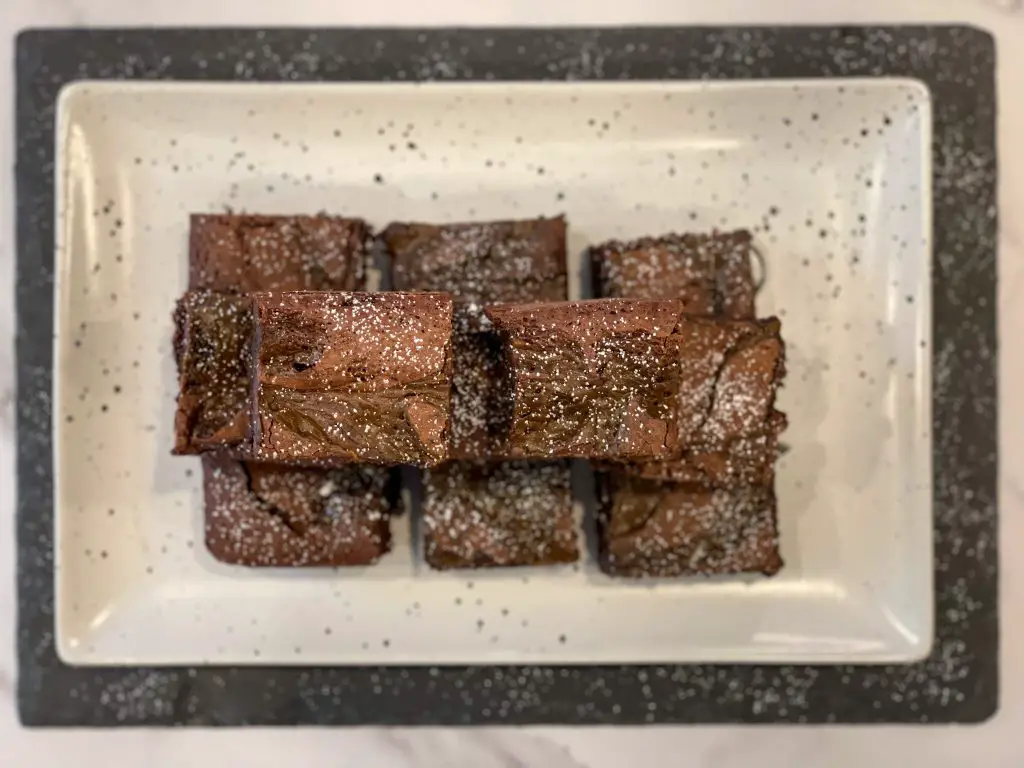 An overhead view of a serving plate of brownies sprinkled with powdered sugar.