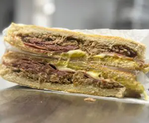 A Cuban sandwich from Social Café wrapped in white paper cut in half.