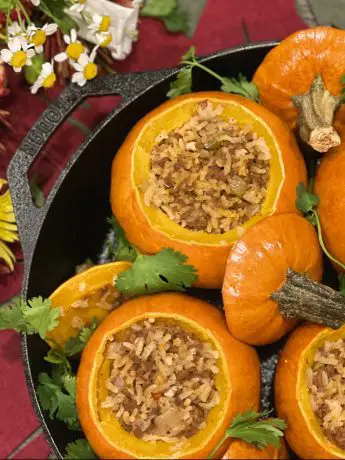 Mini rice and Picadillo stuffed pumpkins presented with cilantro and fresh flowers in a cast iron skillet.
