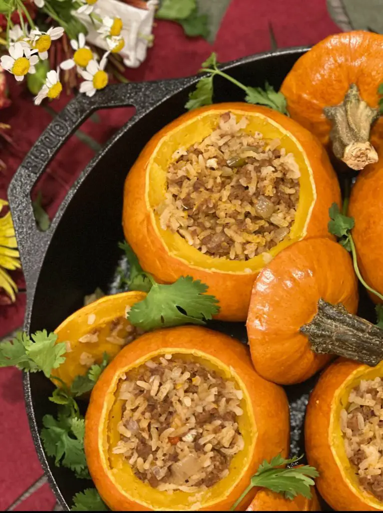 Mini rice and Picadillo stuffed pumpkins presented with cilantro and fresh flowers in a cast iron skillet.