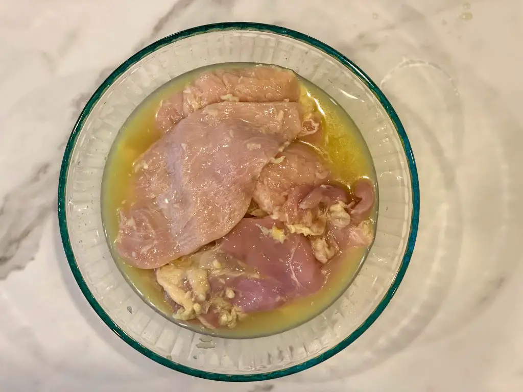 Chicken marinating in a glass bowl.