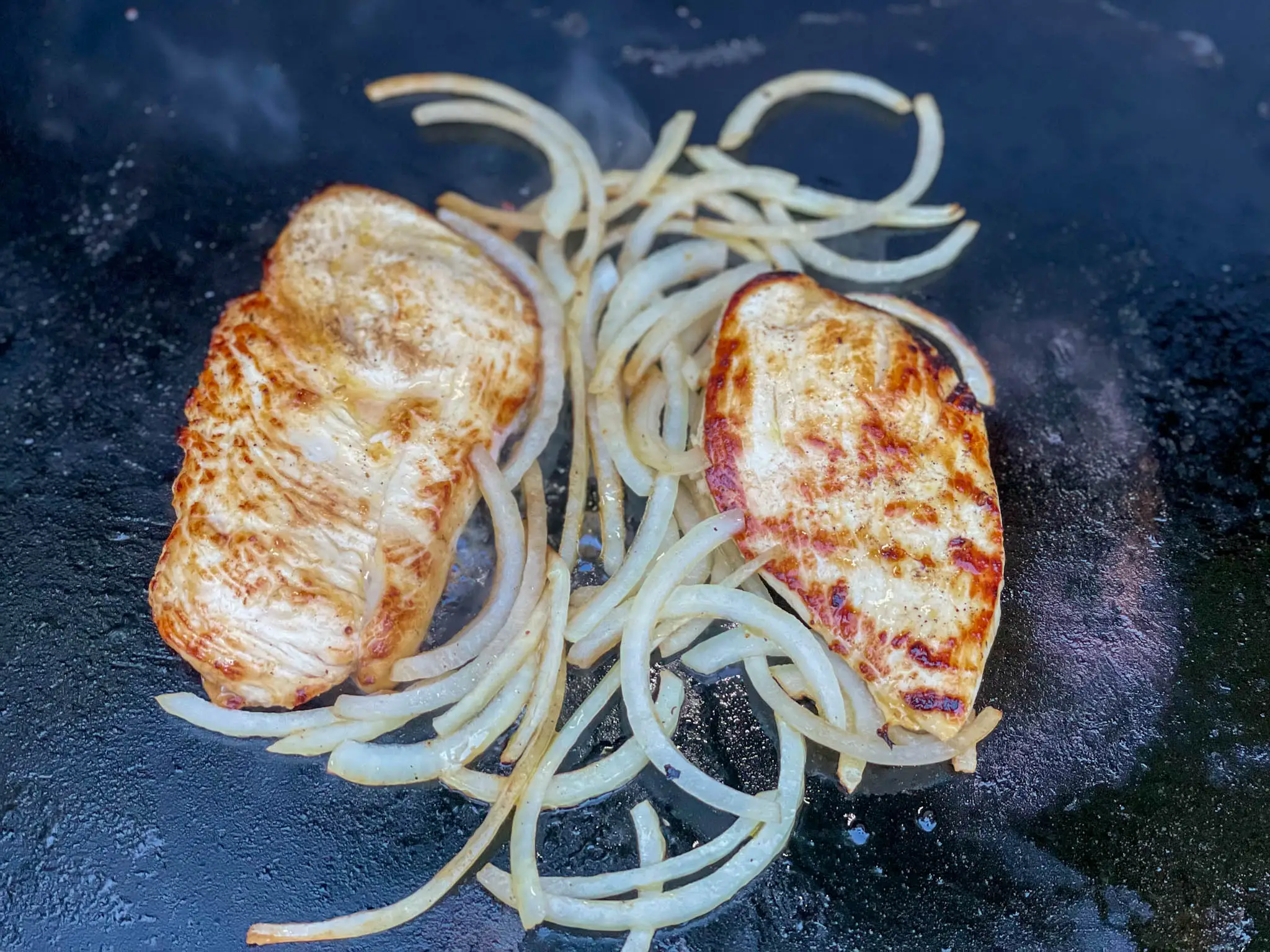 Chicken cooking with onions on a griddle.