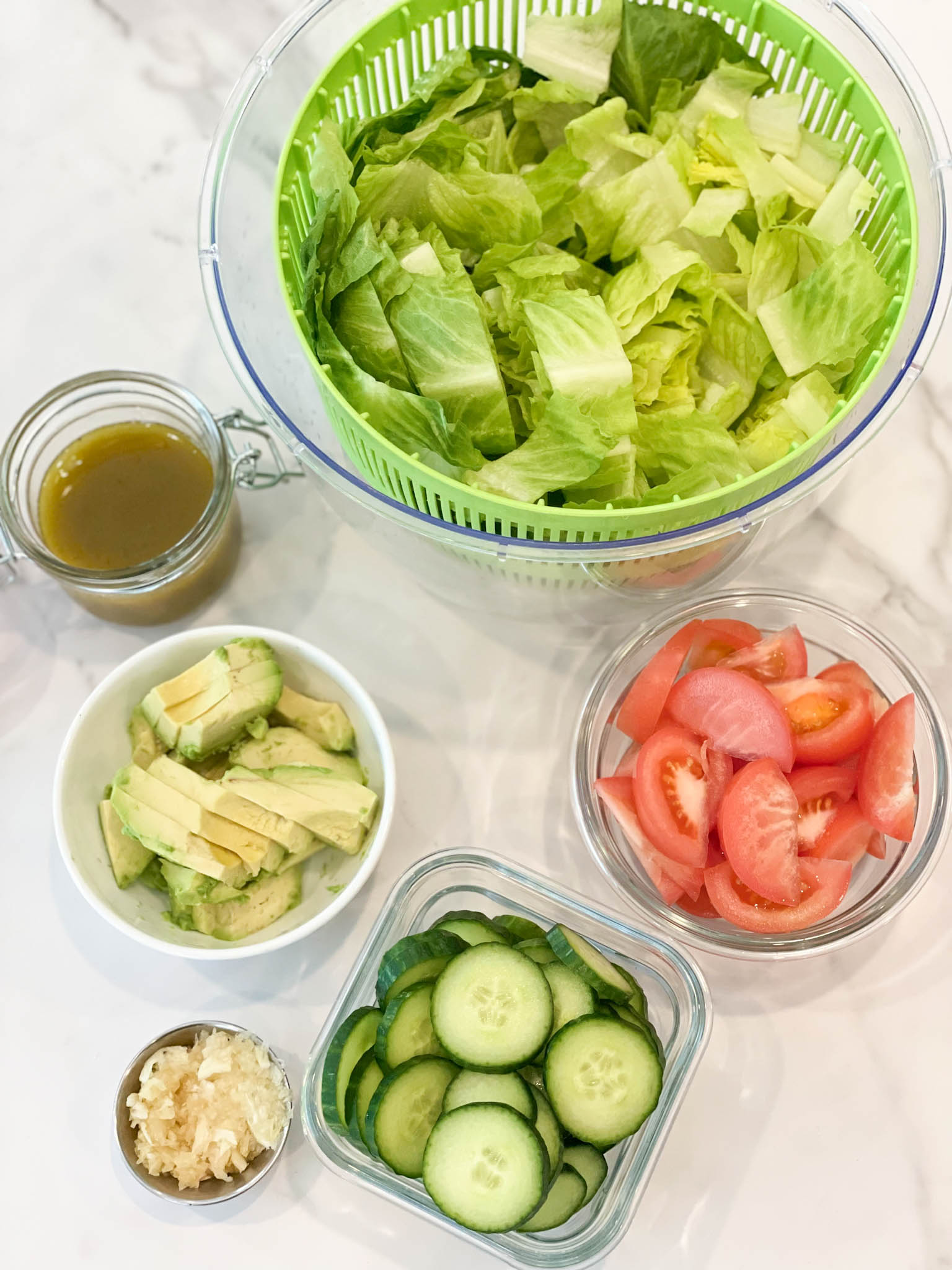 Ingredients for a salad. Cucumbers, tomatoes, fresh garlic, avocados, vinaigrette and romaine lettuce in separate bowls.