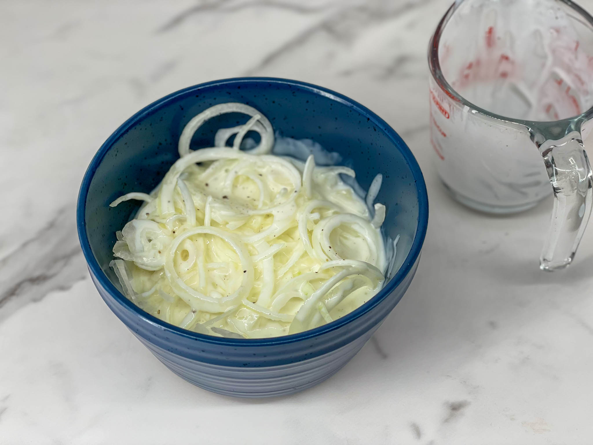 Onion slices marinating in buttermilk in a blue bowl.