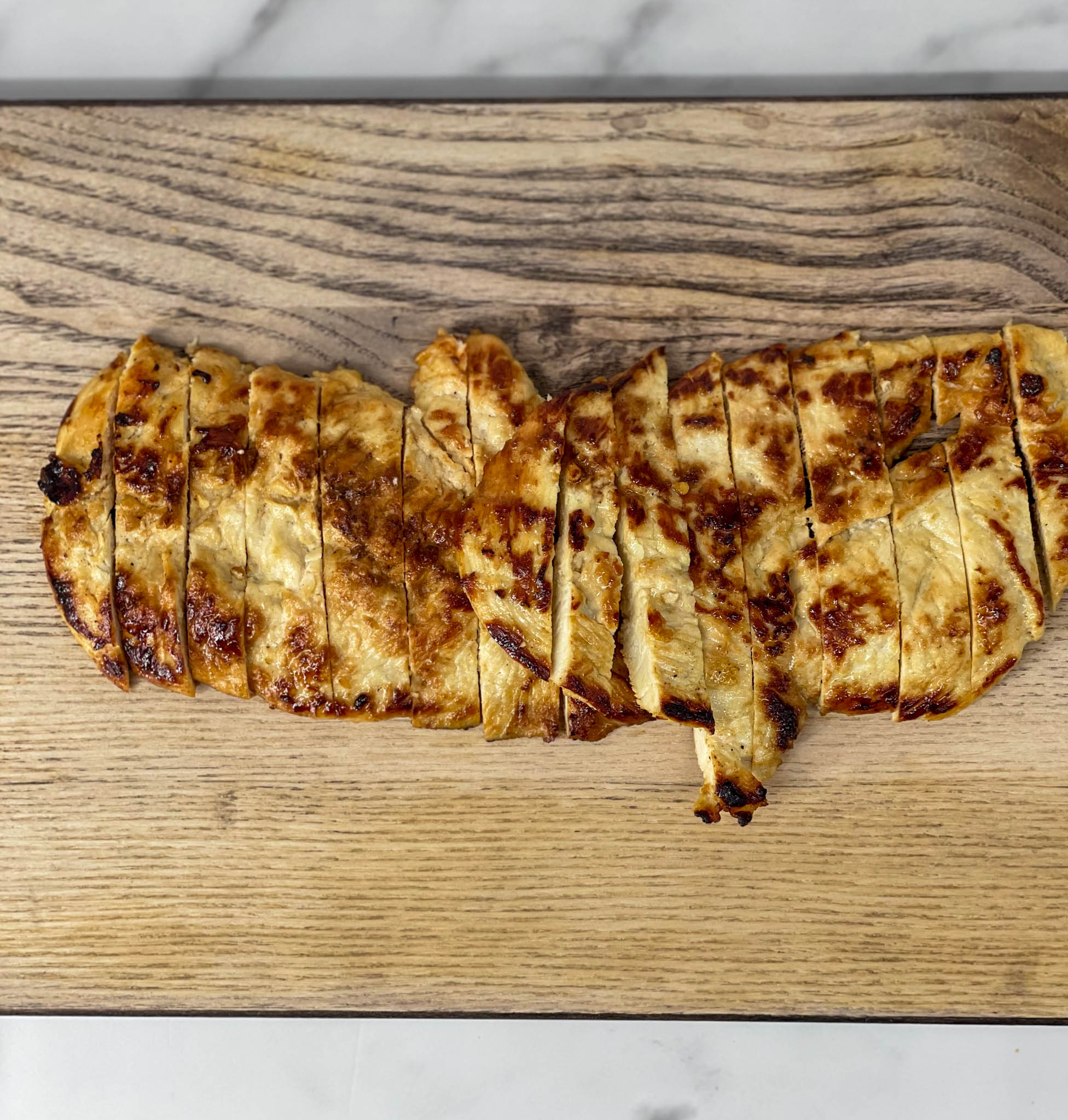 Grilled chicken on a wooden cutting board.