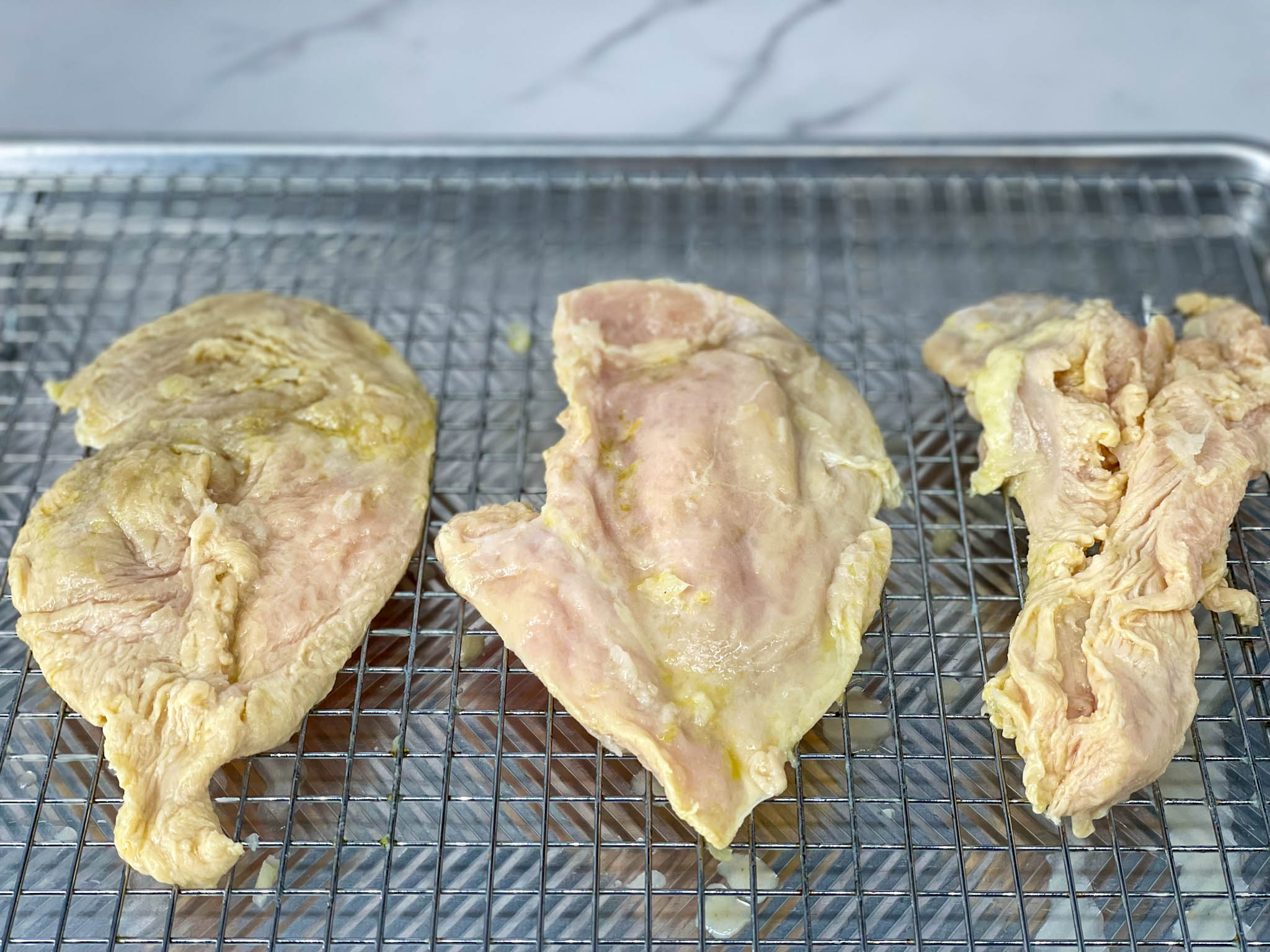Chicken breast that has been marinated in naranja agria, lime juice and garlic on a wire rack.