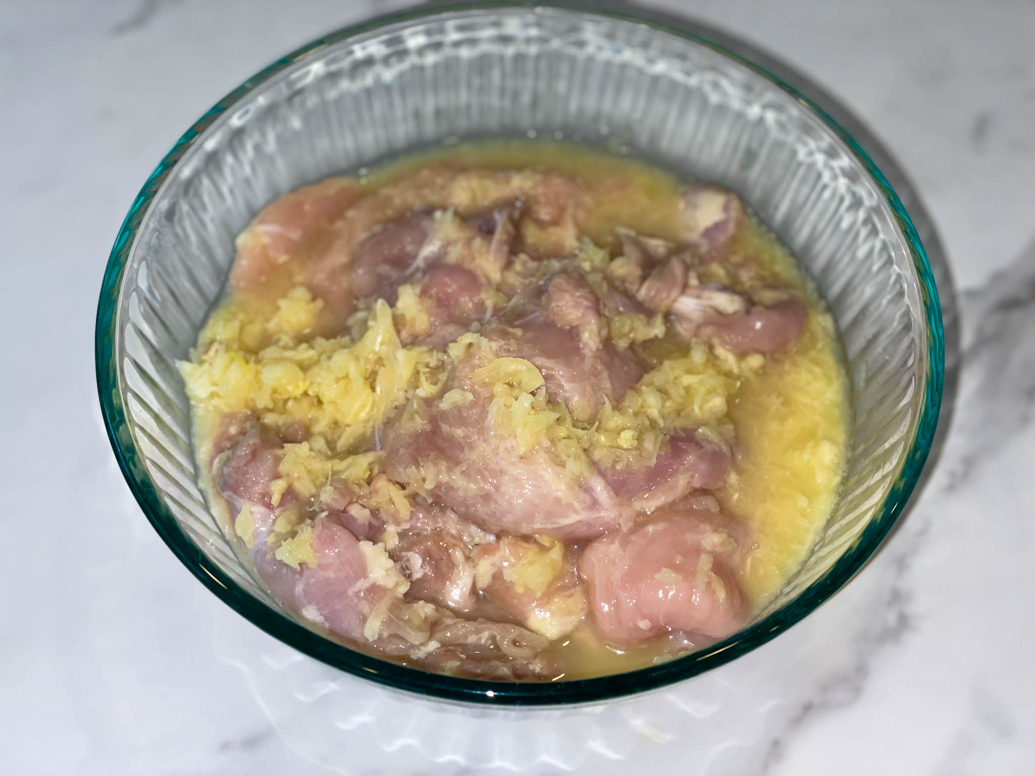Raw chicken breast marinating in naranja agria, lime juice and garlic in a glass bowl on a white background.