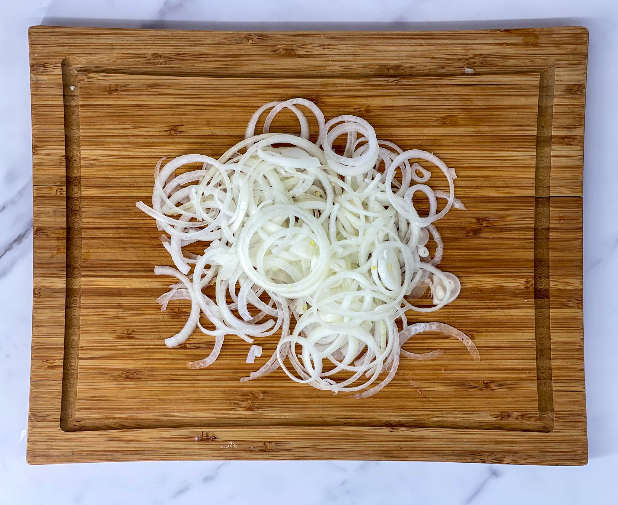 Thinly sliced onions on wooden cutting board with a white background.